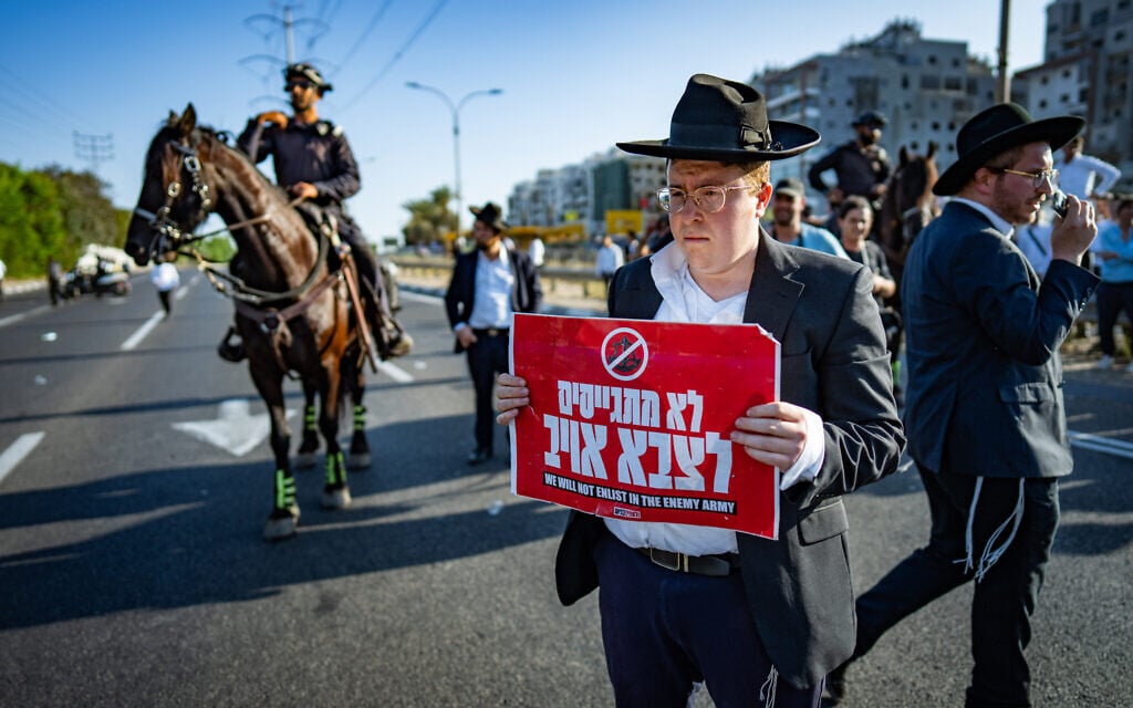 An ultra-Orthodox man holds a sign reading, "We won't be recruited to an enemy army," during a protest against the recruitment of Haredim to the military, on Route 4 near Bnei Brak, June 5, 2025. (Erik Marmor/Flash90)