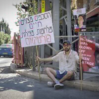 An Israeli protester sits outside Prime Minister Benjamin Netanyahu's residence, calling for the return of the Israeli hostages and an end to the war, on June 13, 2025. His sign reads: "Agreements save lives. Wars save politicians." (Rachel Alroey/FLASH90)