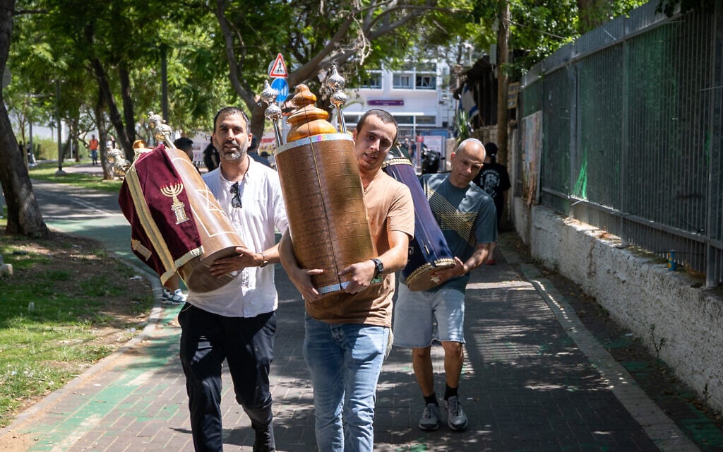 Israelis remove Torah scrolls from a synagogue after a ballistic missile fired from Iran landed in Holon, June 19, 2025 (Chaim Goldberg/Flash90)
