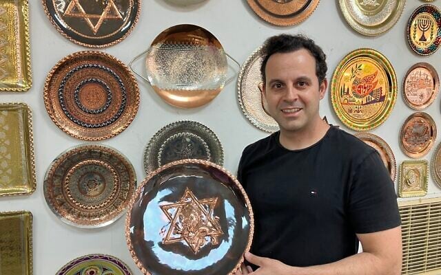 Dror Miro, a fourth-generation coppersmith, holds his 'Rising Lion' plate he designed and made in the old city of Acre on June 16, 2025. (Diana Bletter/Times of Israel)