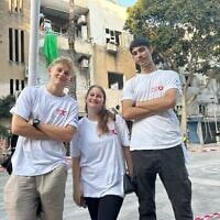 Lev Echad volunteers (from left) Ray Margolin, May Esher, and Eyal Meidan, stand against a background of buildings damaged by an Iranian missile on June 22, 2025. (Sue Surkes/Times of Israel)