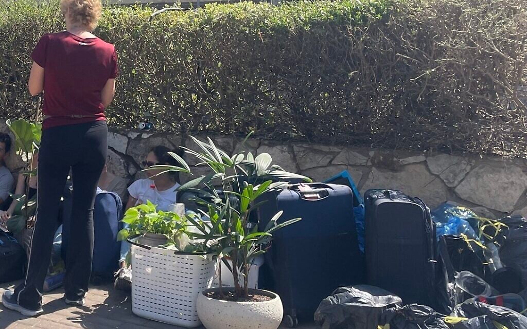 Students wait for a truck to take suitcases and potted plants from a building damaged during an Iranian missile attack on the northern city of Haifa on June 15, 2025, photographed on June 16, 2025. (Sue Surkes/Times of Israel)