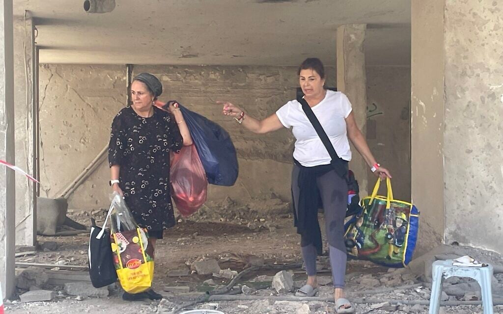 Two women carry shopping bags full of belongings from an apartment in a building next to which an Iranian missile exploded on June 15, 2025, photographed on June 16, 2025. (Sue Surkes/Times of Israel)