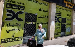 A woman walks past the closed offices of the Alkhalej Exchange Company in Ramallah on May 16, 2024. (JAAFAR ASHTIYEH / AFP)