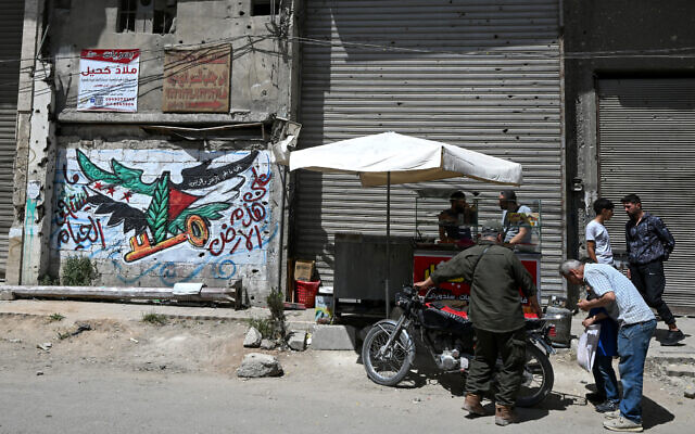 Men check a motorbike next to a mural painting bearing an image of the Syrian and Palestinian flags with a key symbolising a lost Palestinian home in what is now Israel, in the Yarmuk camp for Palestinian refugees in southern Damascus on May 22, 2025. (Louai Beshara/AFP) Men check a motorbike next to a mural painting bearing an image of the Syrian and Palestinian flags with a key symbolising a lost Palestinian home in what is now Israel, in the Yarmuk camp for Palestinian refugees in southern Damascus on May 22, 2025. (Louai Beshara/AFP)