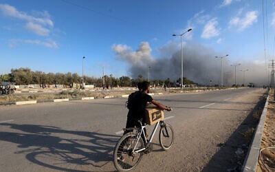Smoke plumes rise during an Israeli strike as a man pushed his bicycle along the Salah al-Din road near the Nusseirat refugee camp in the central Gaza Strip, used by food-seeking Palestinians to reach an aid distribution point set up by the privately-run Gaza Humanitarian Foundation (GHF), on June 25, 2025. (Eyad BABA / AFP)