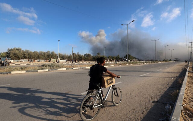 Smoke plumes rise during an Israeli strike as a man pushed his bicycle along the Salah al-Din road near the Nusseirat refugee camp in the central Gaza Strip, used by food-seeking Palestinians to reach an aid distribution point set up by the privately-run Gaza Humanitarian Foundation (GHF), on June 25, 2025. (Eyad BABA / AFP) Smoke plumes rise during an Israeli strike as a man pushed his bicycle along the Salah al-Din road near the Nusseirat refugee camp in the central Gaza Strip, used by food-seeking Palestinians to reach an aid distribution point set up by the privately-run Gaza Humanitarian Foundation (GHF), on June 25, 2025. (Eyad BABA / AFP)