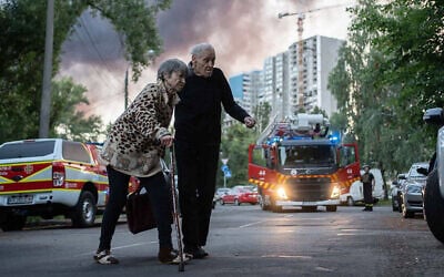 An elderly couple crossing a street as smoke rises in the background at a site of a strike following a mass Russian drone and missile attack on the Ukraine's capital Kyiv, July 4, 2025. (Handout / STATE EMERGENSY SERVICE OF UKRAINE / AFP)