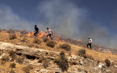 Illustrative: Palestinians run across a hill as they try to chase off violent settlers in the West Bank village of Sinjil, July 4, 2025. (JOHN WESSELS / AFP)