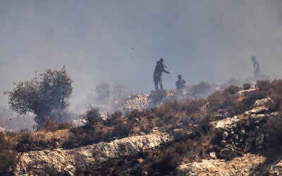 Masked settlers hurl rocks at Palestinians from the top of a hill in the West Bank village of Sinjil, July 4, 2025. (JOHN WESSELS / AFP)