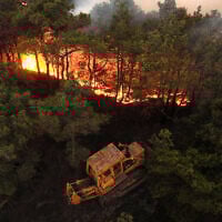 This handout picture released by the Syrian Arab News Agency's (SANA) telegram page shows a bulldozer attempting to contain a wildfire sweeping through Qatal Maaf in the Latakia province in Syria's Mediterranean West on July 4, 2025. (SANA / AFP)