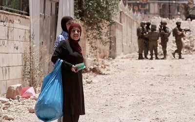 Palestinian women carry their belongings as Israeli soldiers enforce an evacuation order on a house in the Jenin refugee camp in the West Bank on July 8, 2025. (Jaafar ASHTIYEH / AFP)