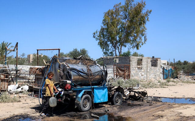 A boy draws water into a jerrycan from the tank of a destroyed mobile water cistern that damaged by an Israeli strike in the Nuseirat camp in the central Gaza Strip on July 14, 2025 (Eyad BABA / AFP)