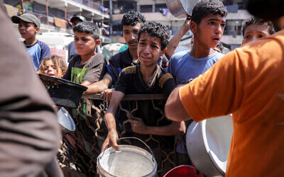 Children queue with pots to receive meals from a charity kitchen in Gaza City on July 14, 2025. (BASHAR TALEB / AFP)