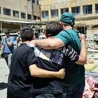 A health worker and other men walk amid the bodies of victims of the recent clashes between local Druze fighters and Bedouin tribes, laid out for identification in the yard of a hospital in Syria's southern city of Sweida on July 17, 2025. (Shadi AL-DUBAISI / AFP)