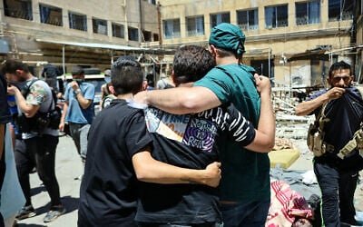A health worker and other men walk amid the bodies of victims of the recent clashes between local Druze fighters and Bedouin tribes, laid out for identification in the yard of a hospital in Syria's southern city of Sweida on July 17, 2025. (Shadi AL-DUBAISI / AFP)
