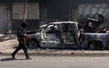 A fighters from Bedouin tribes walks past a burnt vehicle in al-Mazraa village in Syria's southern Sweida governorate, July 18, 2025. (Bakr ALKASEM / AFP)