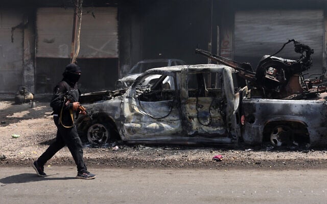 A fighters from Bedouin tribes walks past a burnt vehicle in al-Mazraa village in Syria's southern Sweida governorate, July 18, 2025. (Bakr ALKASEM / AFP)