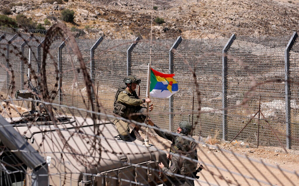 Israeli army soldiers fix a Druze flag attached to the antenna of an army humvee at a position along the barbed-wire fence near the Druze village of Majdal Shams in the Golan Heights on July 19, 2025. (Jalaa MAREY / AFP)