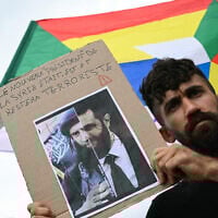 A protestor holds a sign reading "The new 'President' of Syria was, is and will stay a terrorist" in front of a Druze flag bearing the Druze star during a demonstration in support of the Syrian Druze community at Place du Trocadero, in Paris on July 19, 2025. (Bertrand GUAY / AFP)