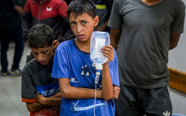 A boy stands holding an intravenous line for an injured man lying on the floor at Nasser Medical Complex in Khan Yunis in the southern Gaza Strip on July 20, 2025. (AFP)
