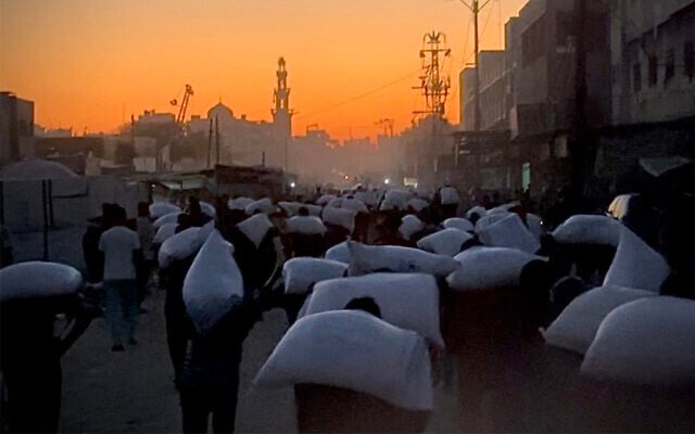 Men walk carrying sacks of flour that were taken from a raided truck carrying foodstuffs, in Khan Younis in the southern Gaza Strip on July 22, 2025. (AFP)