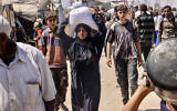 A Palestinian woman carries a bag of food on her head in the al-Mawasi camp in Rafah in the southern Gaza Strip, July 27, 2025. (AFP)
