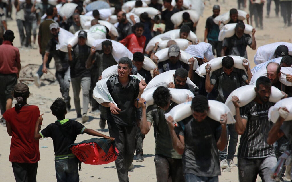 Illustrative: Palestinians carry sacks of flour near Jabalia, in the northern Gaza Strip, on July 27, 2025, after trucks carrying humanitarian aid entered into northern Gaza. (BASHAR TALEB / AFP)