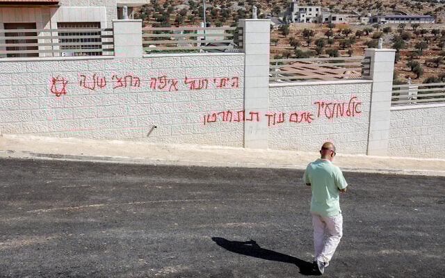 A man walks past Hebrew graffiti reading 'Al-Mughayyir, you'll be sorry,' following a Jewish extremist attack on the Palestinian Christian village of Taybeh, northeast of Ramallah in the West Bank, July 28, 2025. (Zain JAAFAR / AFP)