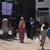 Palestinians carry containers for water at a camp for the displaced in Deir al-Balah, Gaza Strip, July 7, 2025. (AP Photo/Abdel Kareem Hana)