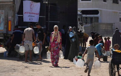 Palestinians carry containers for water at a camp for the displaced in Deir al-Balah, Gaza Strip, July 7, 2025. (AP Photo/Abdel Kareem Hana)
