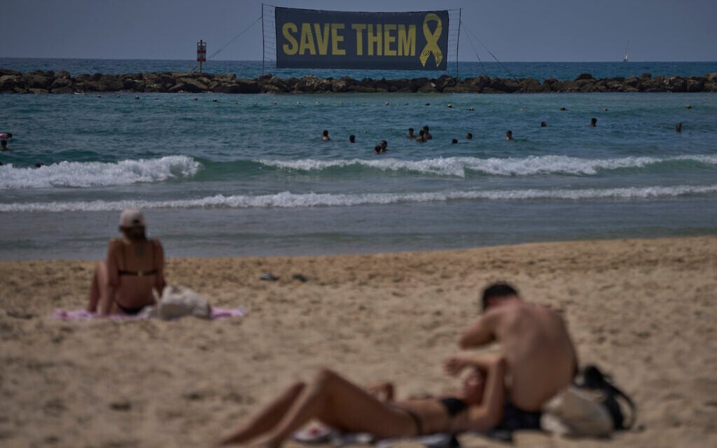A banner, referring to the hostages being held by Palestinian terrorists in the Gaza Strip, is displayed on the beach as people enjoy the seaside, in Tel Aviv, July 10, 2025. (AP Photo/Ohad Zwigenberg)