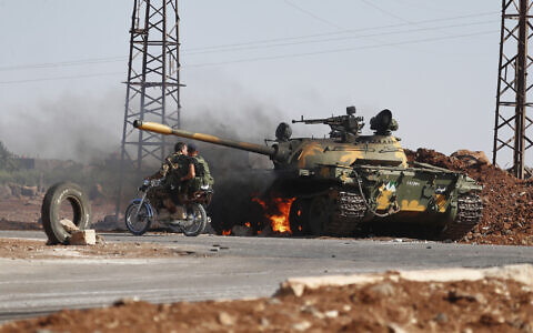 Syrian government soldiers on a motorcycle pass by a burning tank on the outskirts of Sweida city, where clashes erupted between Druze militias and Sunni Bedouin clans, in southern Syria, July 14, 2025. (AP/Omar Sanadiki)