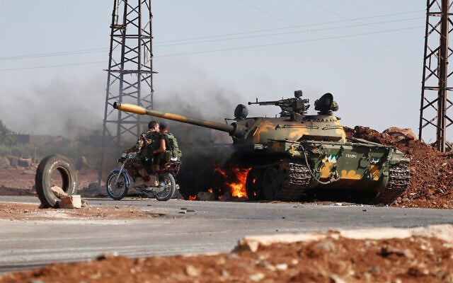Syrian government soldiers on a motorcycle pass by a burning tank on the outskirts of Sweida city, where clashes erupted between Druze militias and Sunni Bedouin clans, in southern Syria, July 14, 2025. (AP/Omar Sanadiki)