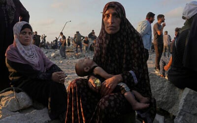 Somoud Wahdan looks at the camera as she sits with her child in an area in the northern Gaza Strip, while waiting for trucks with humanitarian aid to arrive, in Gaza City, Friday, July 25, 2025. (AP Photo/Abdel Kareem Hana)