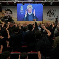 People raise their fists as Hezbollah leader Naim Qassem delivers a televised speech in Dahiyeh, a southern suburb of Beirut, Lebanon, July 30, 2025, during a commemoration marking the first anniversary of the death of top Hezbollah commander Fuad Shukr, who was killed in an Israeli airstrike. (AP Photo/Bilal Hussein)