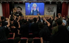People raise their fists as Hezbollah leader Naim Qassem delivers a televised speech in Dahiyeh, a southern suburb of Beirut, Lebanon, July 30, 2025. (AP Photo/Bilal Hussein)