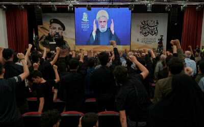 People raise their fists as Hezbollah leader Naim Qassem delivers a televised speech in Dahiyeh, a southern suburb of Beirut, Lebanon, July 30, 2025, during a commemoration marking the first anniversary of the death of top Hezbollah commander Fuad Shukr, who was killed in an Israeli airstrike. (AP Photo/Bilal Hussein)
