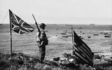 American and Canadian flags fly on top of a hill while a US soldier stands guard, overlooking part of the invasion fleet, as troops rush supplies and ammunition ashore during the occupation of Kiska Island, Alaska on October 12, 1943. (AP Photo)