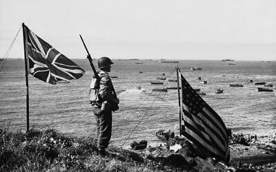 American and Canadian flags fly on top of a hill while a US soldier stands guard, overlooking part of the invasion fleet, as troops rush supplies and ammunition ashore during the occupation of Kiska Island, Alaska on October 12, 1943. (AP Photo)