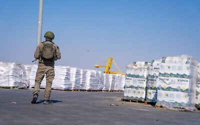 A soldier stands near aid packages on the Gazan side of the Kerem Shalom Crossing, in the southern Gaza Strip, July 24, 2025. (Emanuel Fabian/Times of Israel)
