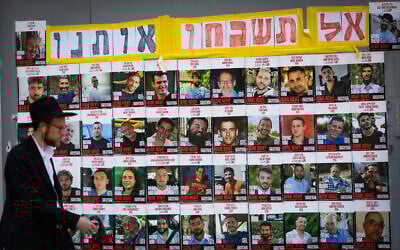 People walking next to pictures of hostages held by terrorists in Gaza, in Jerusalem, July 2, 2025 (Yonatan Sindel/Flash90)