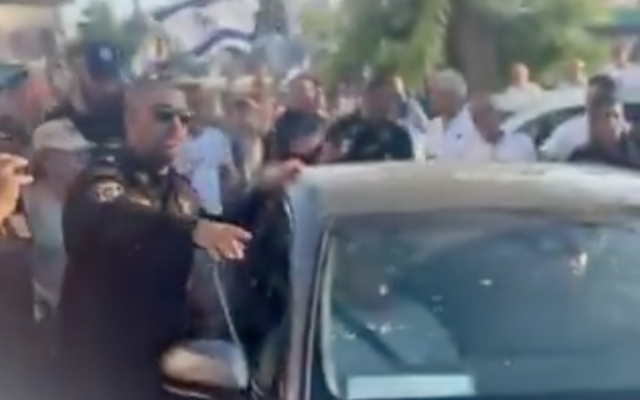 A policeman escorts a car carrying MK Ayman Odeh as right-wing demonstrators surround the vehicle in Ness Ziona, July 19, 2025. (X screenshot used in accordance with article 27a of the Copyright Law)
