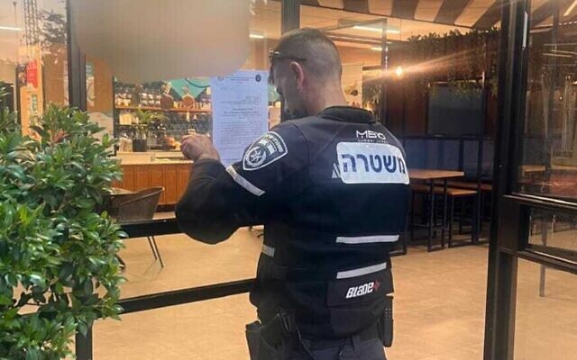 A policeman puts a closure order on a Tel Aviv University cafe, July 27, 2025. (Israel Police)