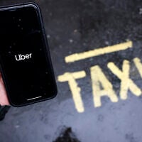 Illustrative: A man holds a smartphone showing the app for ride-sharing service Uber in London, on March 17, 2021. (Tolga Akmen / AFP)