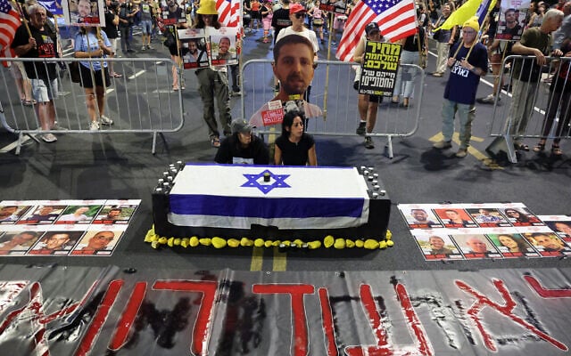 Enav Zangauker (R), mother of Israeli hostage Matan Zangauker, sits with a friend by a fake coffin during an anti-government protest calling for action to secure the release of Israeli hostages held captive since the Hamas-led October 7, 2023, attack in front of the defense ministry in Tel Aviv on August 12, 2025. (Jack GUEZ / AFP)