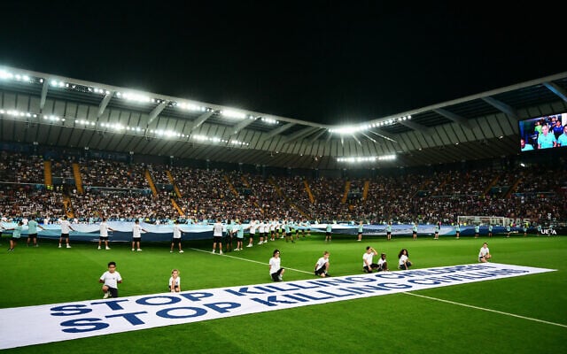 Mascots hold a banner which reads "Stop killing children, Stop killing civilians" on the pitch ahead of the 2025 UEFA Super Cup final football match between Paris Saint-Germain (FRA) and Tottenham Hotspur FC (ENG) at the Friuli stadium, in Udine, on August 13, 2025. (Photo by Marco BERTORELLO / AFP)