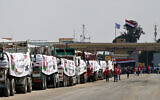 People walk past trucks loaded with aid for Gaza waiting on the Egyptian side of the Strip's Rafah crossing on August 18, 2025. (Khaled DESOUKI / AFP)