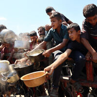 Palestinian boys extend their empty pots to receive cooked rice from charity kitchen in Gaza City on August 23, 2025. (Omar AL-QATTAA / AFP)