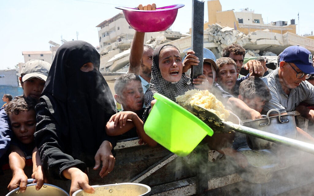 Palestinians extend their empty pots to receive cooked rice from a charity kitchen in Gaza City, on August 23, 2025. (Omar AL-QATTAA / AFP) Palestinians extend their empty pots to receive cooked rice from a charity kitchen in Gaza City, on August 23, 2025. (Omar AL-QATTAA / AFP)